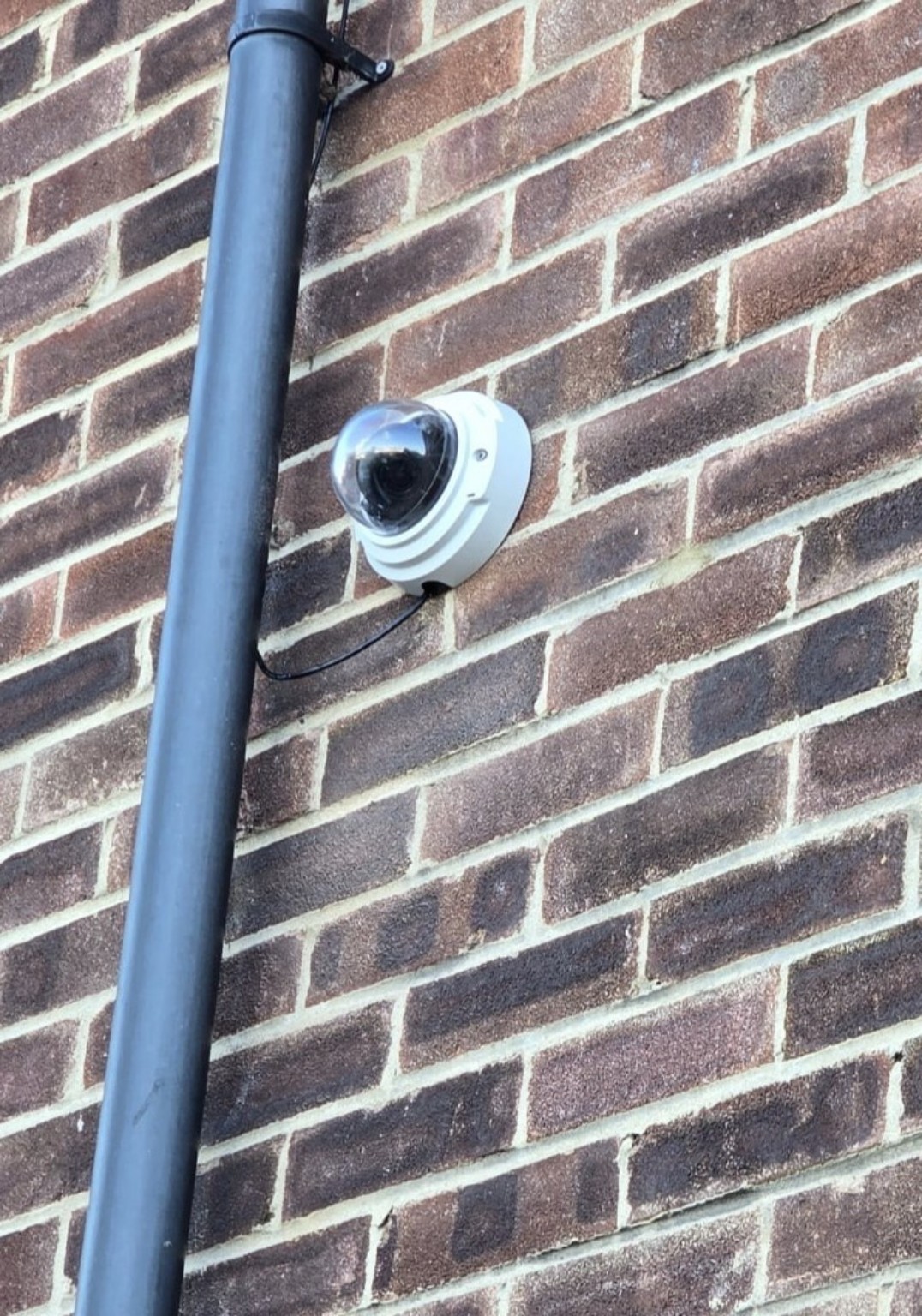 Real dome CCTV camera mounted on a brick wall beside a downpipe